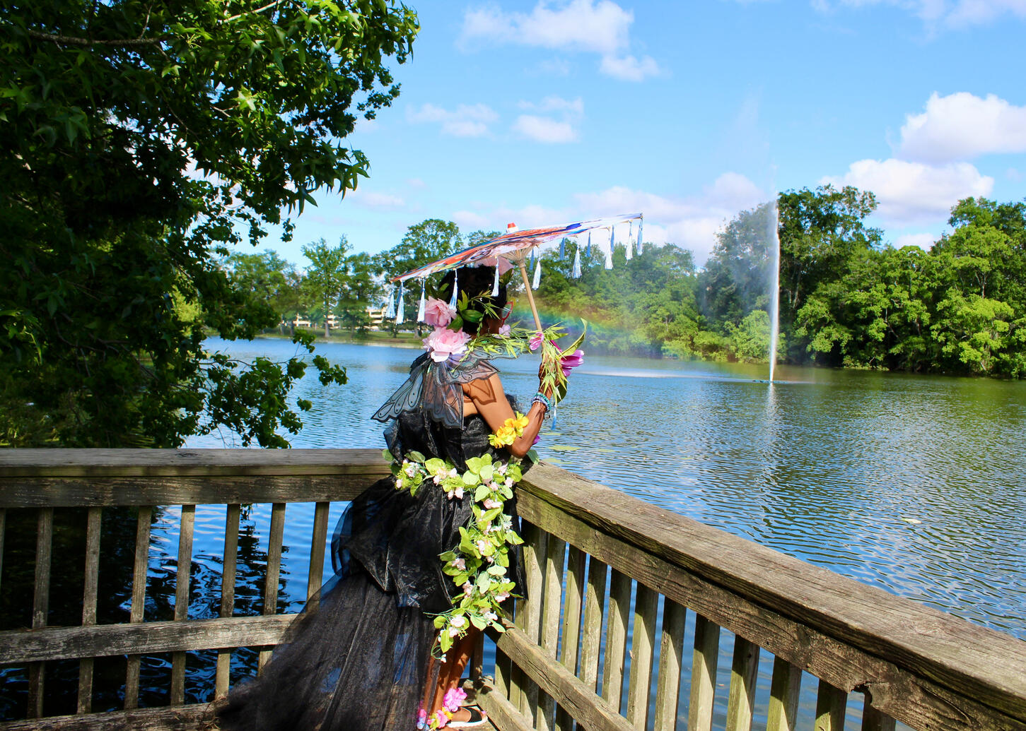 vie from the back of gorgeous Dark fae clad in dark tule and foliage holding an umbrella looking over the water from the pier.