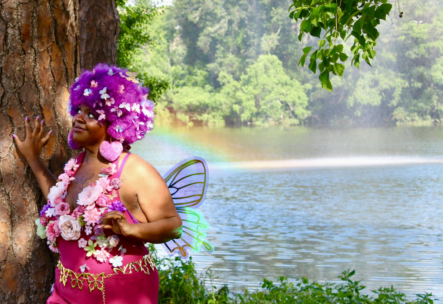 blossoming black fae looking to the sky with lake in background with rainbow behind.
