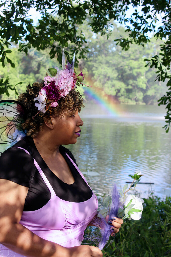 Fae profile in front of lake with rainbow behind her.