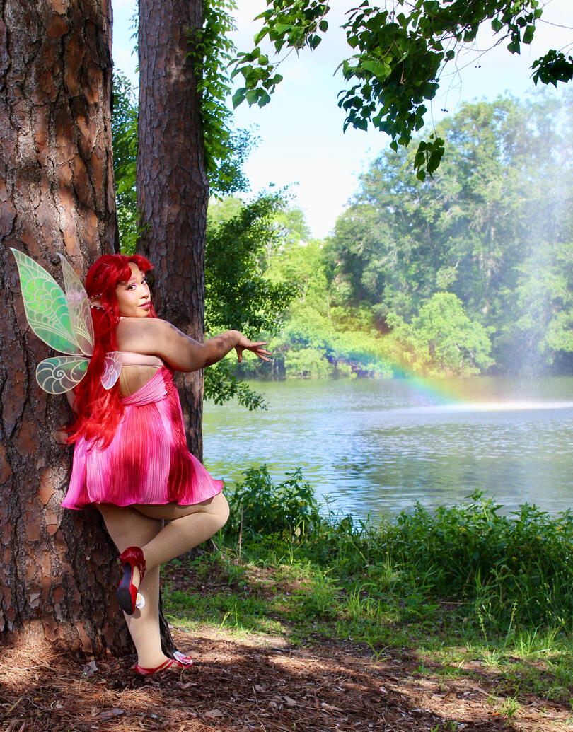 strawberry fairy with hands outstretched to the water in front and one leg up behind her as she looks to the camera over her shoulder.